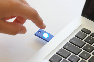 Picture of hand tapping a U2F token inserted in a computer's USB port