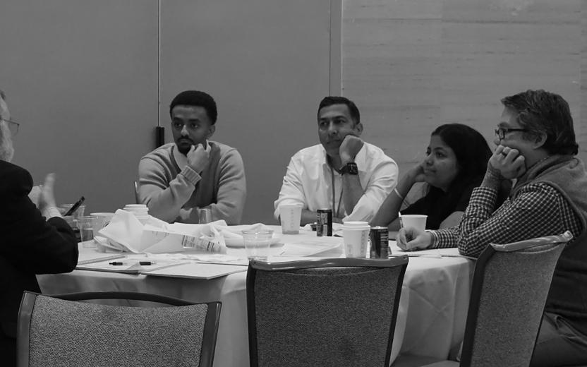 a small group around a table stares at a speaker at the end of a long day