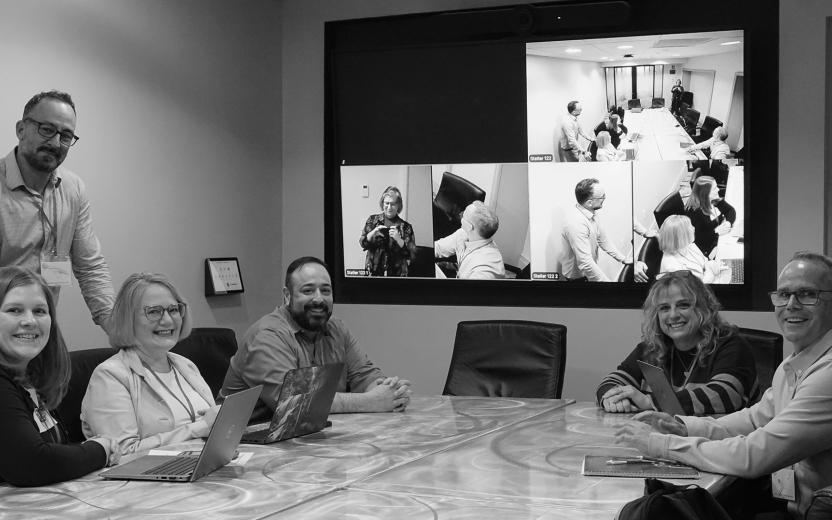 six colleagues smile for a photo in the middle of a small group discussion