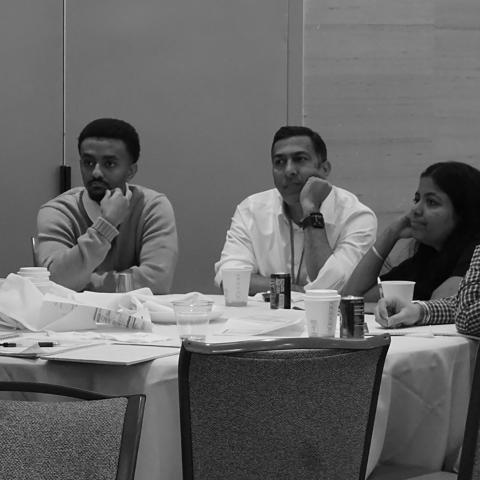 a small group around a table stares at a speaker at the end of a long day