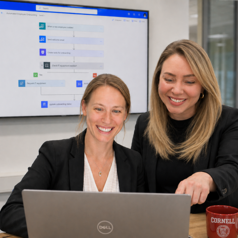 two co-workers look at a laptop where they are improving work processes through automation
