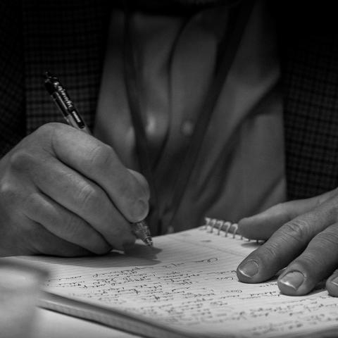 a black and white photo of a man's hand holding a pen while writing in a notebook